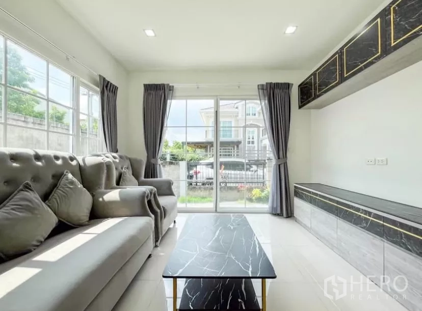 บ้าน ให้เช่าในChom Thong, Bangkok - ห้องนั่งเล่นเปิดออกสู่สวนหน้าบ้านผ่านประตูกระจกบานเลื่อนพร้อมผ้าม่าน
