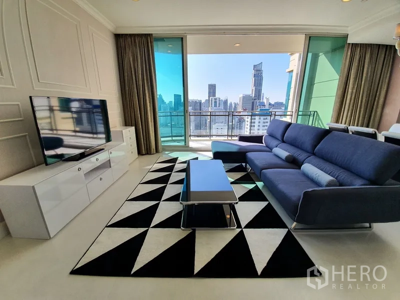 公寓 出租在Watthana, Bangkok - 明亮客厅，海军蓝沙发与几何地毯，电视柜，推拉门连通可观赏曼谷天际线的阳台。