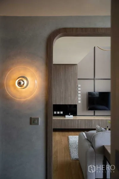 Condominium for sale in Khlong Toei, Bangkok - Entry arch with wall sconce leading to a modern living room with TV wall, wood floors, and built-in cabinet.