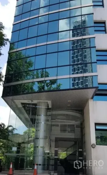 办公空间 出租在Khlong Toei, Bangkok - 办公楼玻璃幕墙入口，倒映天际线，带雨棚与立柱。