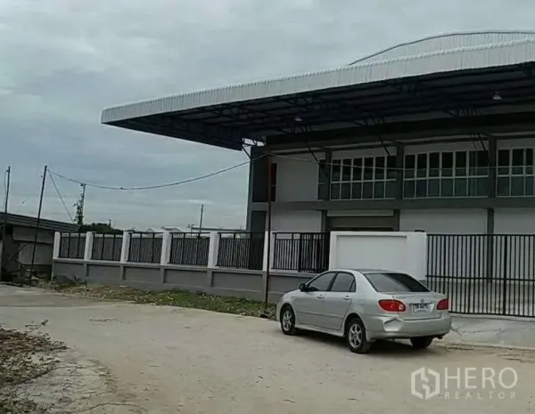 Warehouse for rent in Bang Bo, Samut Prakan - Side view of the fenced warehouse compound with a long overhang roof and road access.