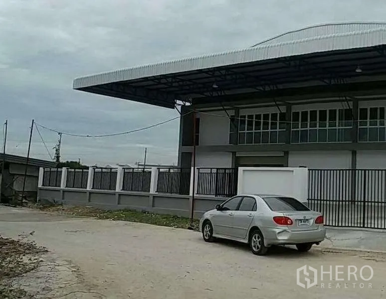 Warehouse for rent in Bang Bo, Samut Prakan - Side view of the fenced warehouse compound with a long overhang roof and road access.