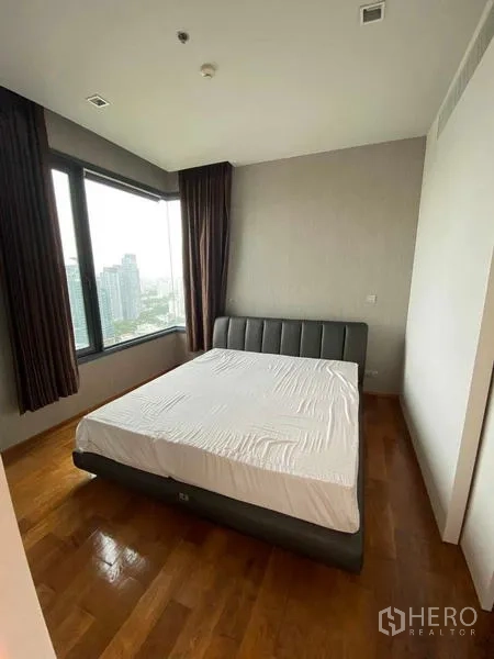 Condominium for rent or sale in Khlong Toei, Bangkok - Master bedroom with queen bed and two large corner windows facing the skyline.
