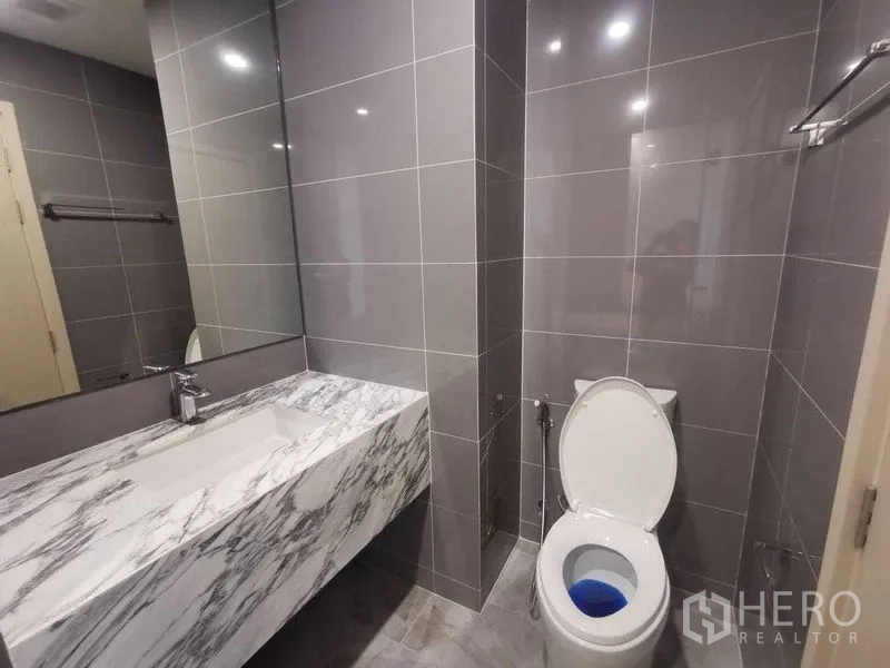 Condominium for rent in Ratchathewi, Bangkok - Modern bathroom with marble vanity and gray tiled walls.