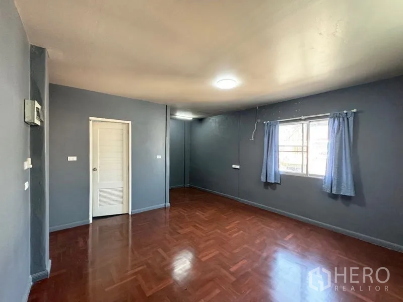 Townhouse for rent or sale in Suan Luang, Bangkok - Large gray-painted room with wood floors and window light