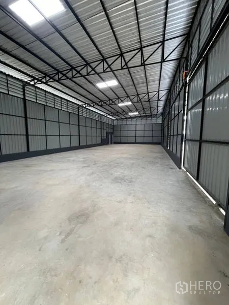 Warehouse for rent in Wang Thonglang, Bangkok - Spacious warehouse interior in Wang Thonglang with high steel truss roof, skylights, and smooth concrete floor.