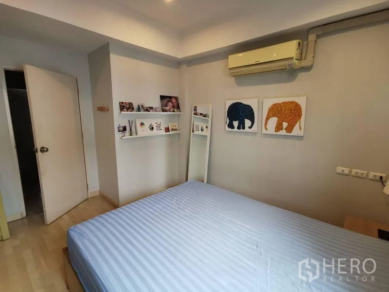 Townhouse for rent or sale in Yan Nawa, Bangkok - Cozy bedroom with wall shelves, elephant artwork and air conditioner.