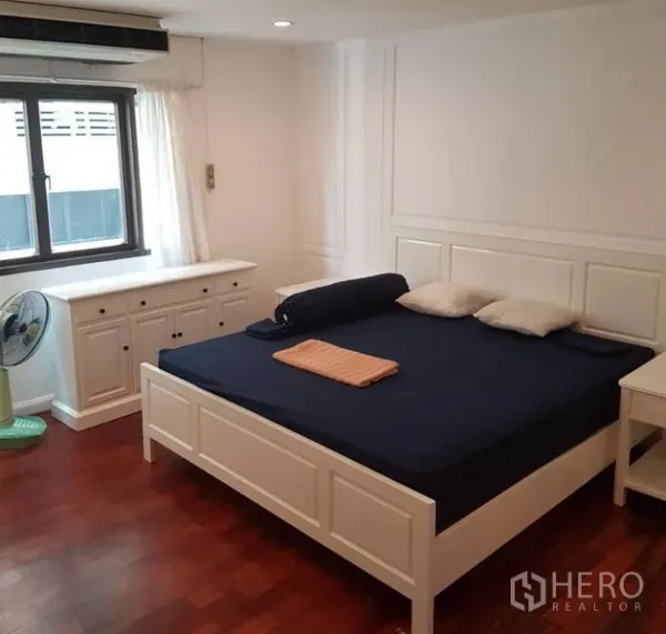 Condominium for rent or sale in Watthana, Bangkok - Bedroom with white bed frame, side tables, dresser and window, set on polished wooden floors.