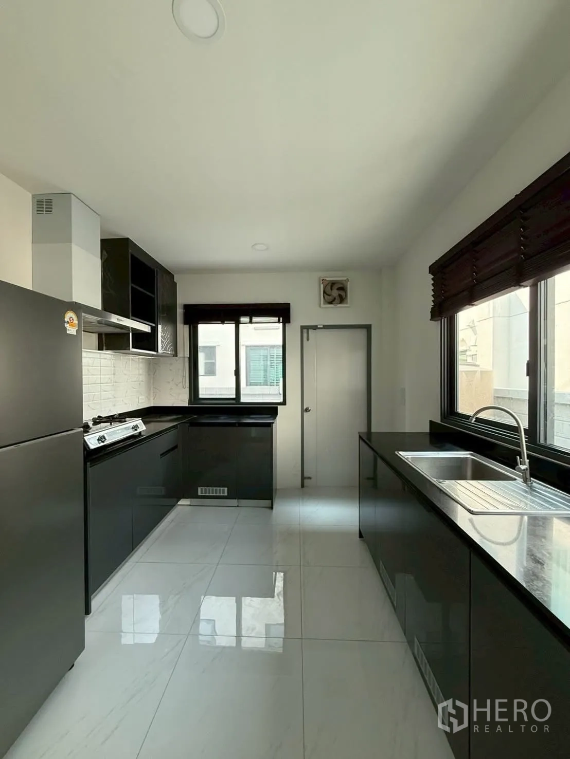 Townhouse for rent - Modern enclosed kitchen with black cabinetry, gas hob, range hood and stainless‑steel sink.