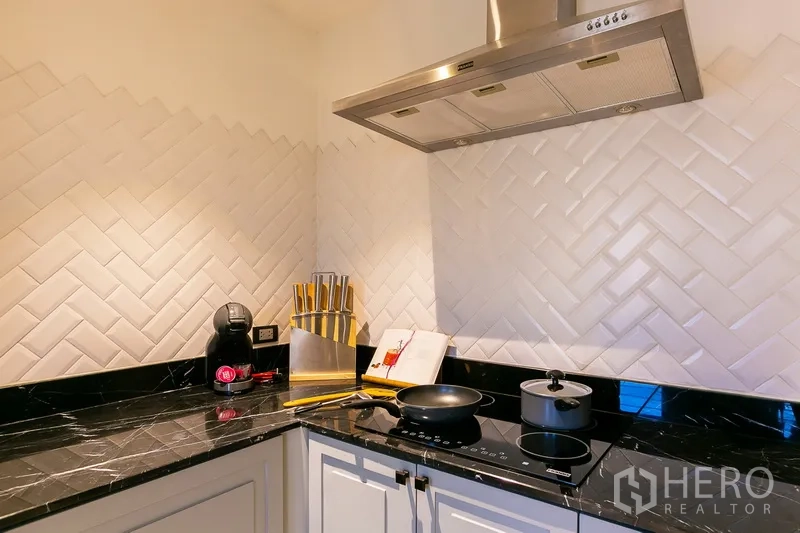 Apartment for rent in Khlong Toei, Bangkok - Modern closed kitchen corner with black stone countertop, induction hob and range hood.