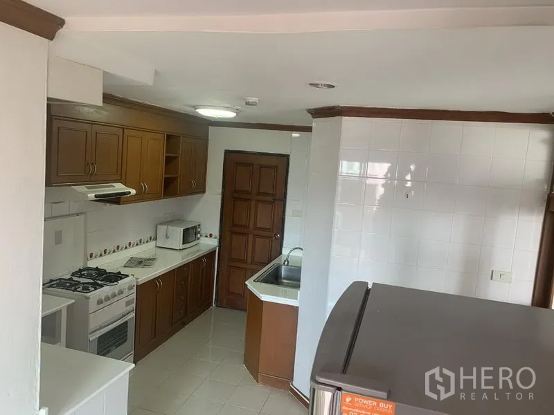 公寓 出租在Watthana, Bangkok - 厨房全景，双水槽、微波炉、瓷砖地面以及通向杂物间的门。