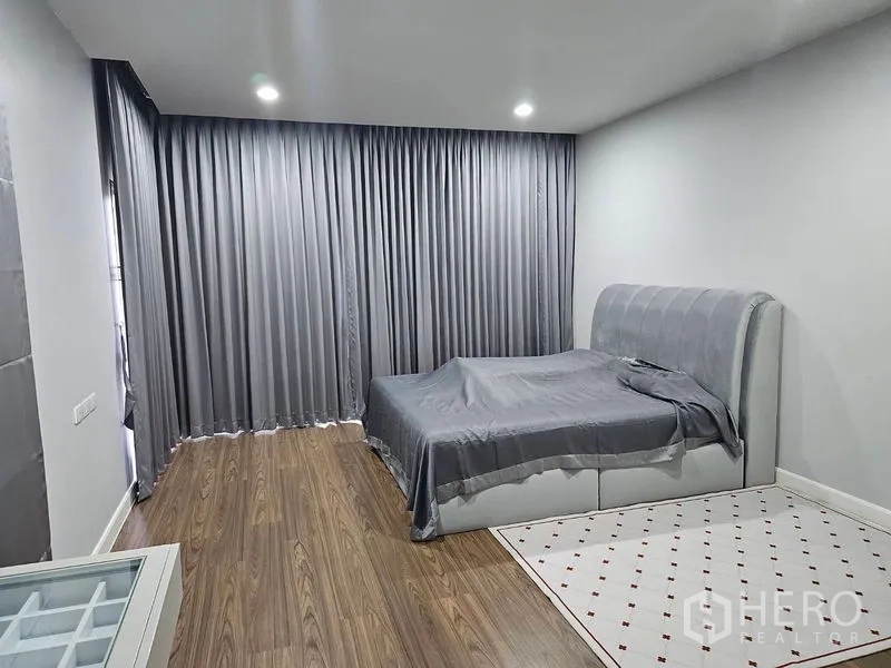 Detached House for rent or sale in Lam Luk Ka, Pathum Thani - Spacious bedroom with gray drapes, upholstered bed and wood floors