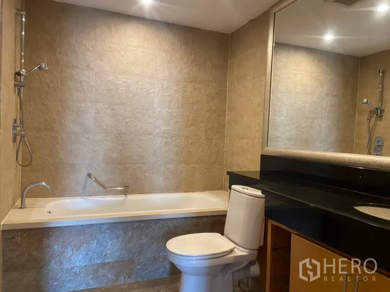 Condominium for rent in Sathon, Bangkok - Bathroom with bathtub, wall shower, large mirror, and stone‑tile finishes.