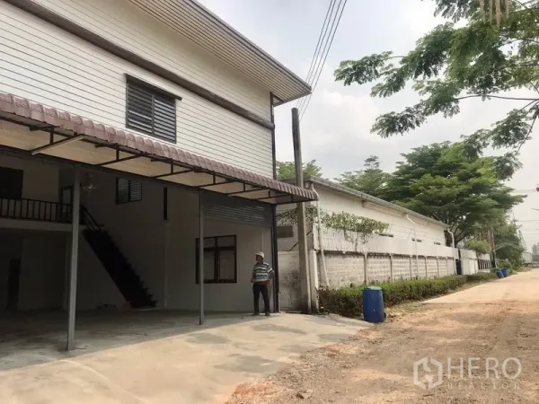 货栈 出租在Pathum Thani - 仓库侧视图，临安静小路，边界绿化成排。