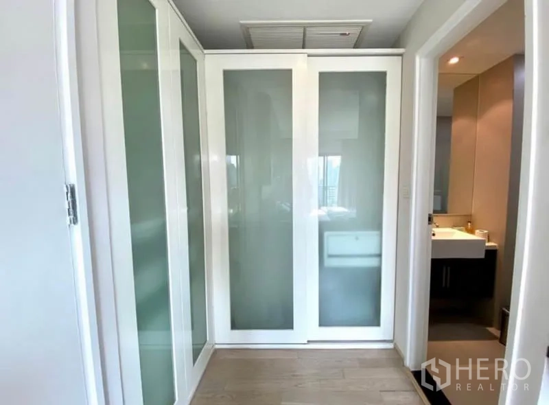 Condominium for rent in Khlong Toei, Bangkok - Walk-in wardrobe with frosted sliding doors leading toward the bathroom.