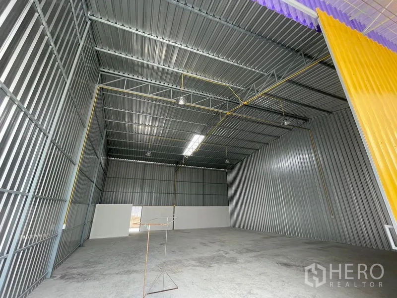 Warehouse for rent in Mueang Nonthaburi, Nonthaburi - Interior of a metal-clad warehouse showing a high gable roof, roof trusses, skylight strip, and concrete floor.