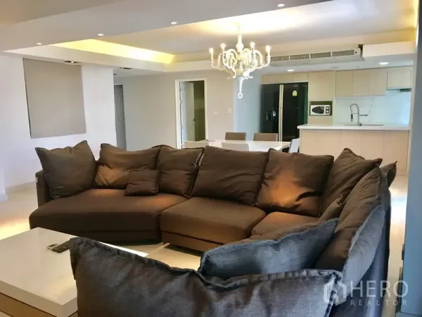 Condominium for rent in Watthana, Bangkok - Cozy living room with large L-shaped sofa, TV feature wall and adjoining kitchen.