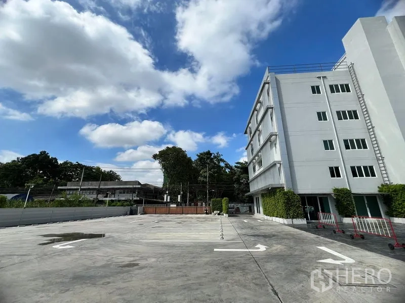 Retail Space for rent in Huai Khwang, Bangkok - Wide parking forecourt beside multi-storey building with street greenery.