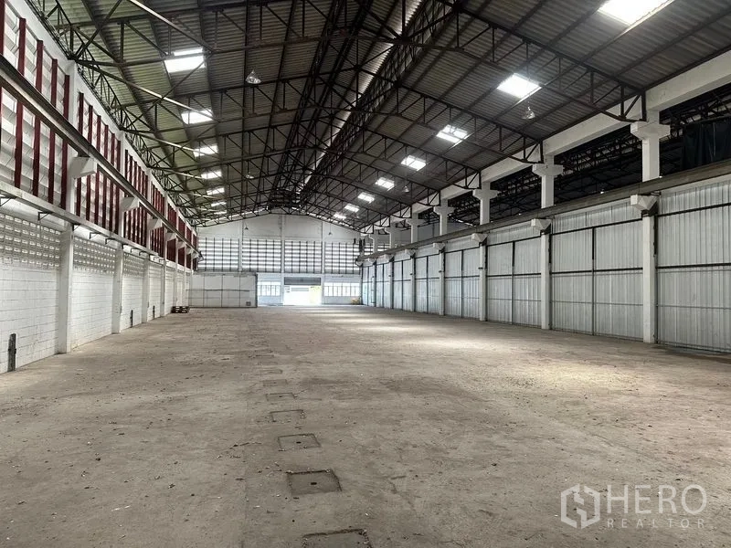 Warehouse for rent in Lam Luk Ka, Pathum Thani - Open warehouse floor facing multiple bays, steel roof with lighting panels, and durable concrete surface.