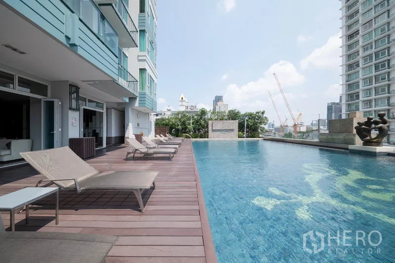 Condominium for rent in Watthana, Bangkok - Outdoor swimming pool with wooden deck, sun loungers, and city backdrop.