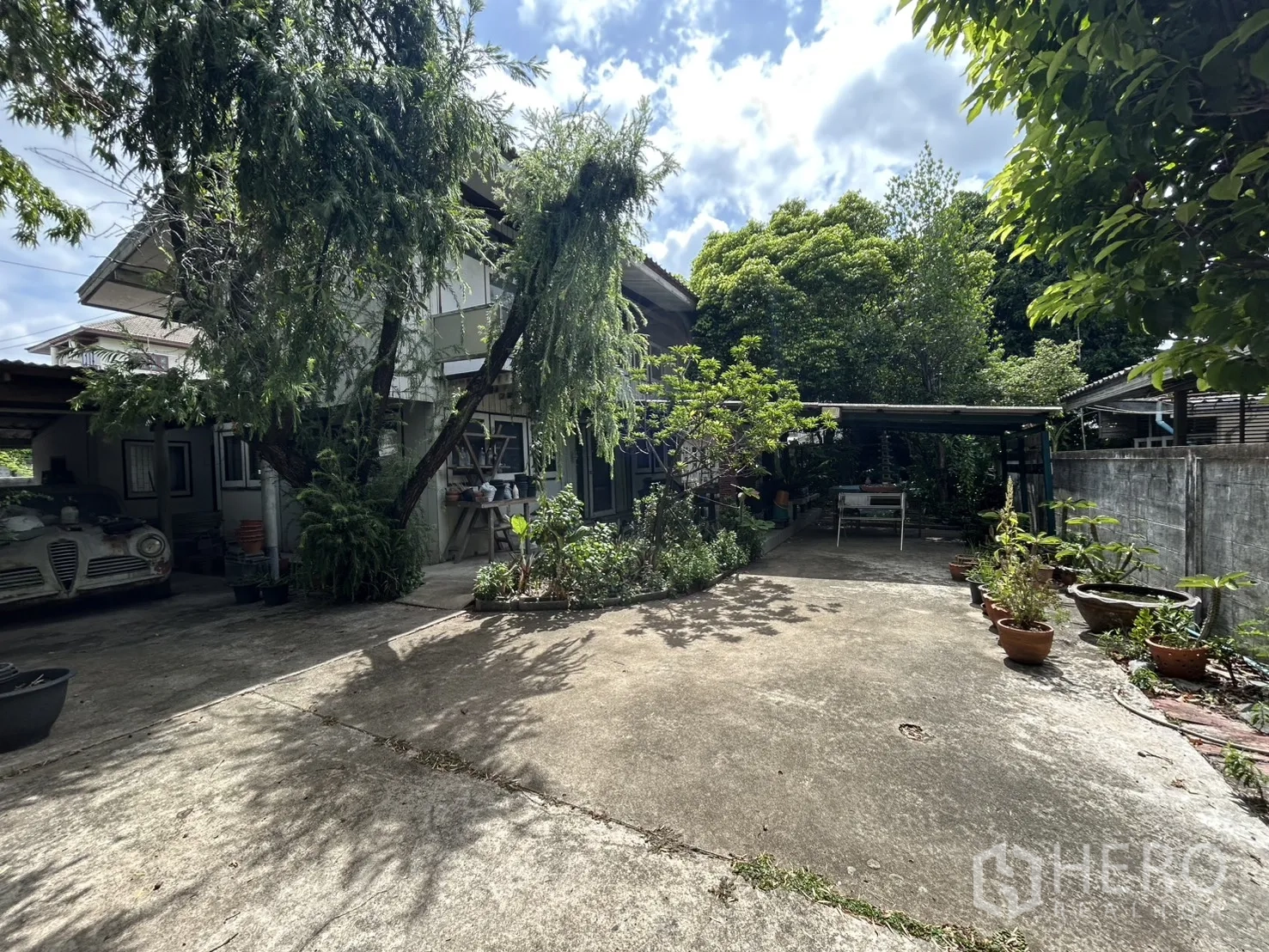 Detached House for sale in Phra Khanong, Bangkok - Front of the house with potted plants, a carport, and a paved area.