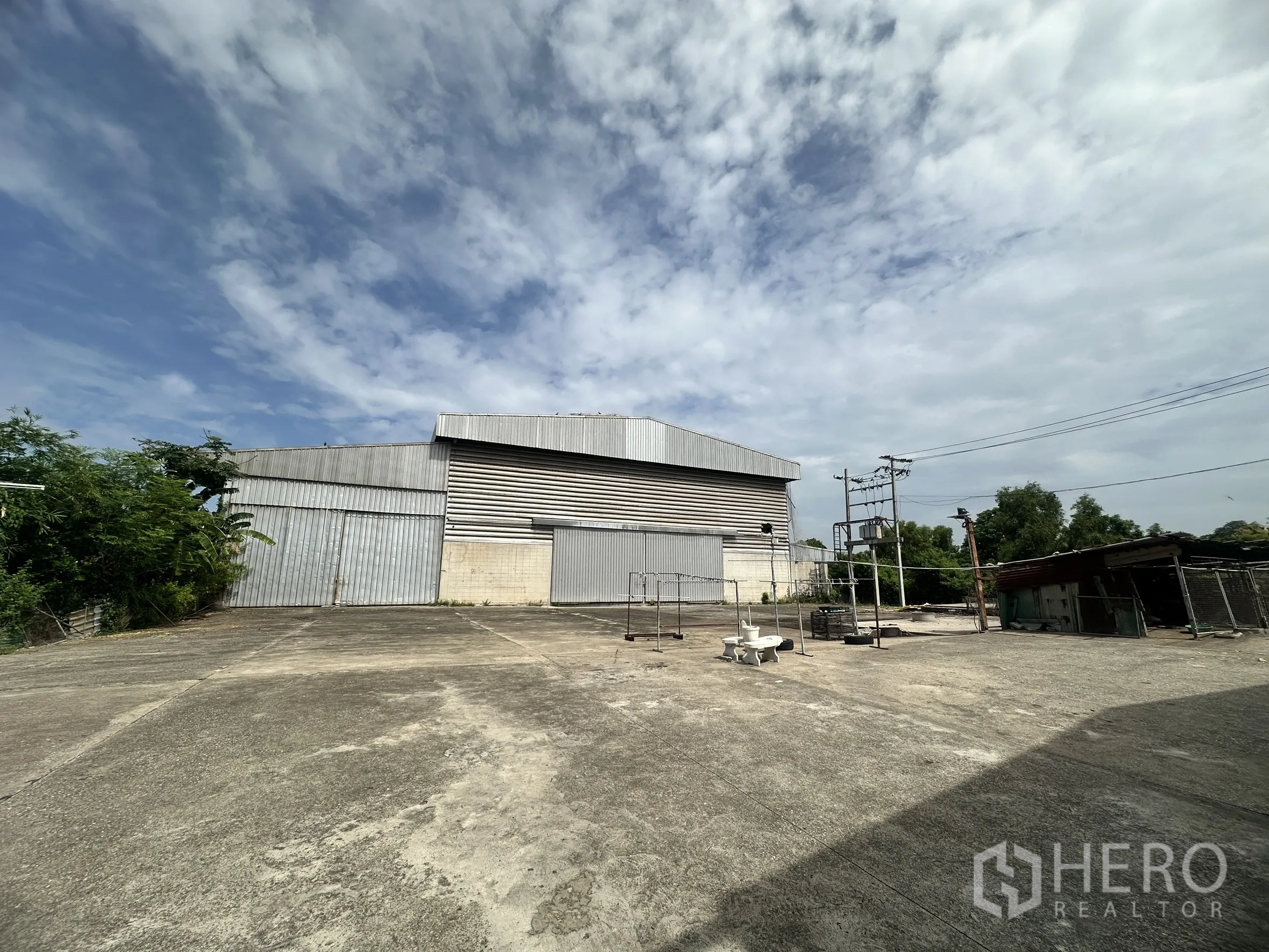 Factory for sale in Sai Noi, Nonthaburi - Corrugated metal warehouse exterior with a broad paved apron.