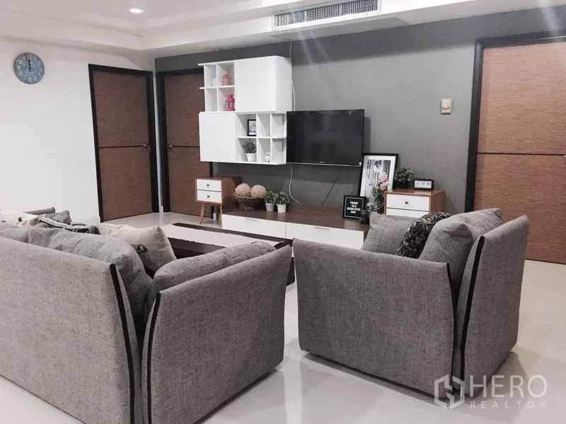 Condominium for rent or sale in Watthana, Bangkok - Living area with wall‑mounted TV, floating shelves, and twin grey sofas facing a coffee table.