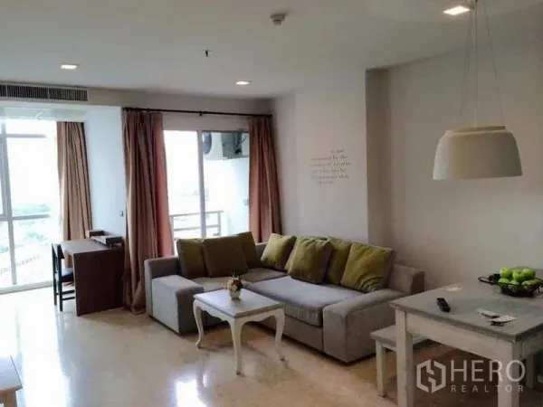 Condominium for rent in Khlong Luang, Pathum Thani - Bright living room with L-shaped sofa, pendant light, work desk and balcony access with city outlook.