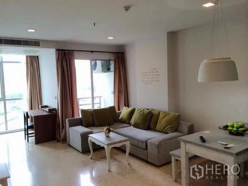 Condominium for rent in Khlong Luang, Pathum Thani - Bright living room with L-shaped sofa, pendant light, work desk and balcony access with city outlook.