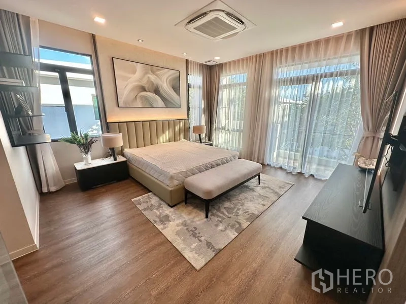 Detached House for rent in Samut Prakan - Bright master bedroom with floor-to-ceiling windows, balcony doors and warm wood flooring.