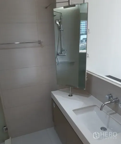 Condominium for rent in Khlong Toei, Bangkok - Contemporary bathroom featuring a sleek vanity, wall-mounted faucet, large mirror and glass shower.