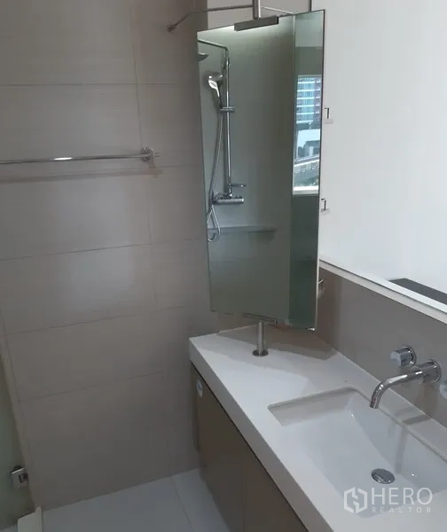 Condominium for rent in Khlong Toei, Bangkok - Contemporary bathroom featuring a sleek vanity, wall-mounted faucet, large mirror and glass shower.