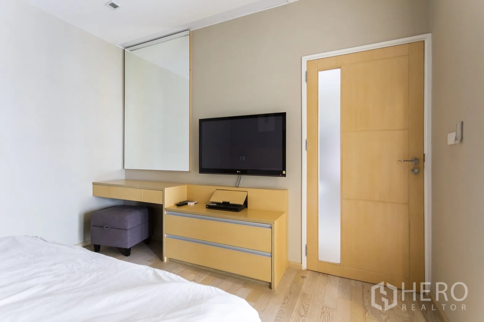 Condominium for rent in Khlong Toei, Bangkok - Bedroom corner with wall-mounted TV, built-in dresser, mirror and light wood door.