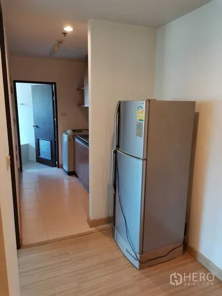 Condominium for rent in Khlong Toei, Bangkok - Hallway with refrigerator leading to a compact kitchen and utility area.
