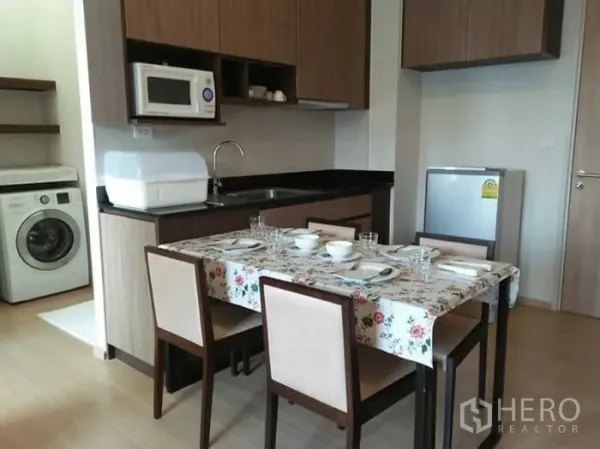 公寓 出租在Huai Khwang, Bangkok - 曼谷公寓的开放式厨房与餐桌，木质橱柜、微波炉、冰箱与洗衣机。