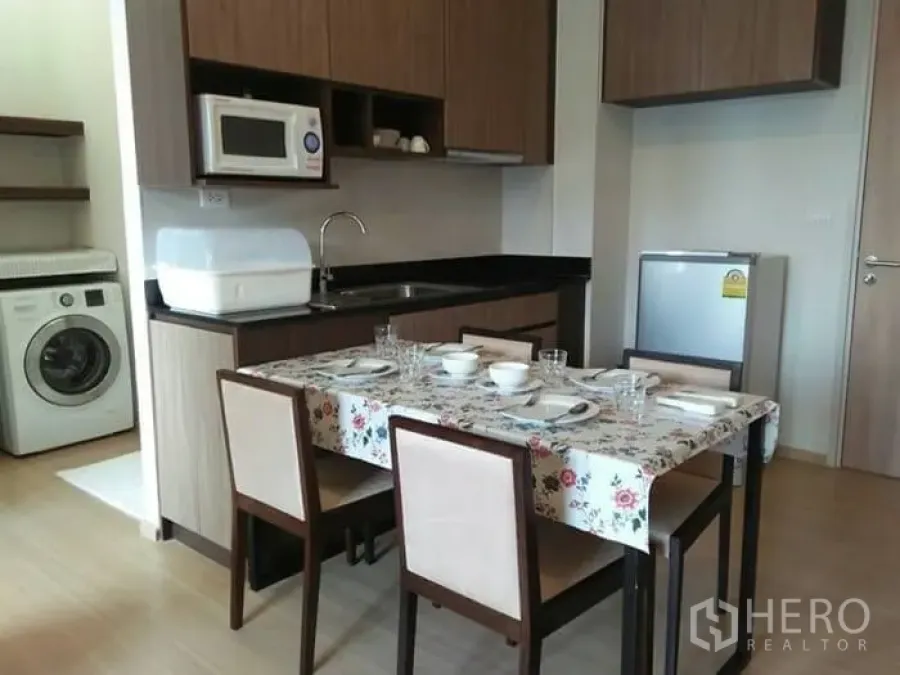 公寓 出租在Huai Khwang, Bangkok - 曼谷公寓的开放式厨房与餐桌，木质橱柜、微波炉、冰箱与洗衣机。