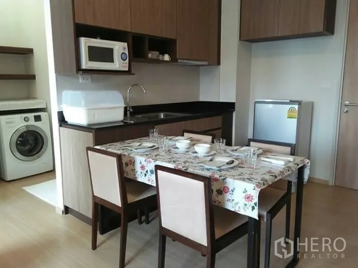 公寓 出租在Huai Khwang, Bangkok - 曼谷公寓的开放式厨房与餐桌，木质橱柜、微波炉、冰箱与洗衣机。