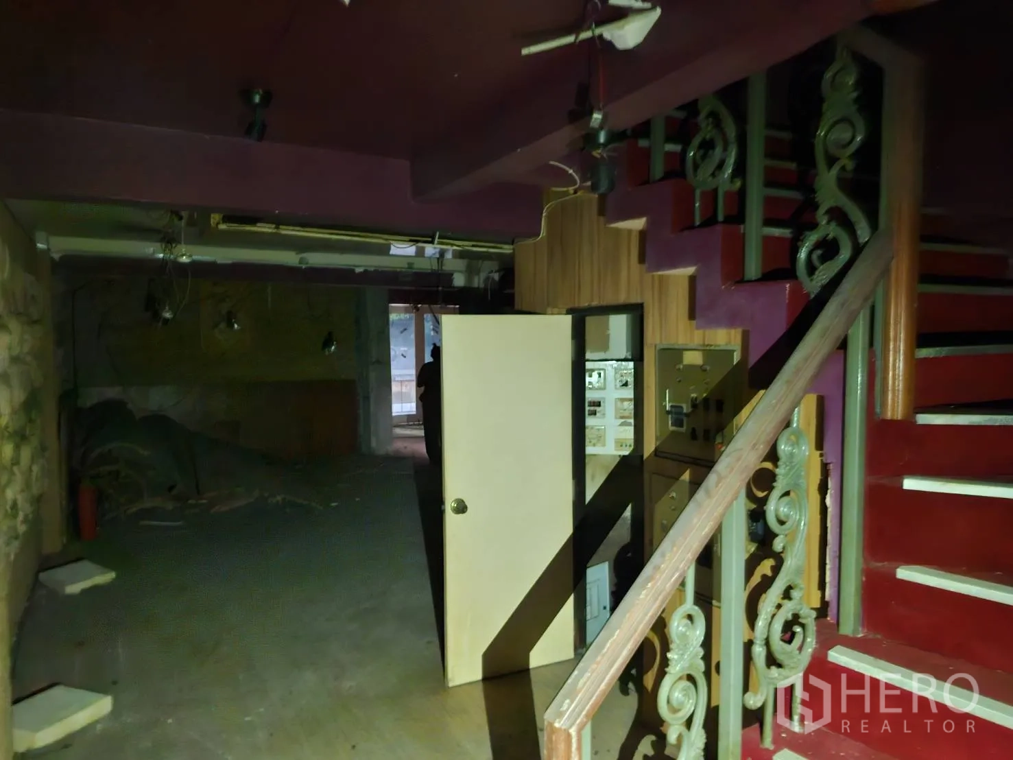Shophouse for rent in Bang Rak, Bangkok - Interior staircase with decorative metal balustrade beside a dark, unused retail area.