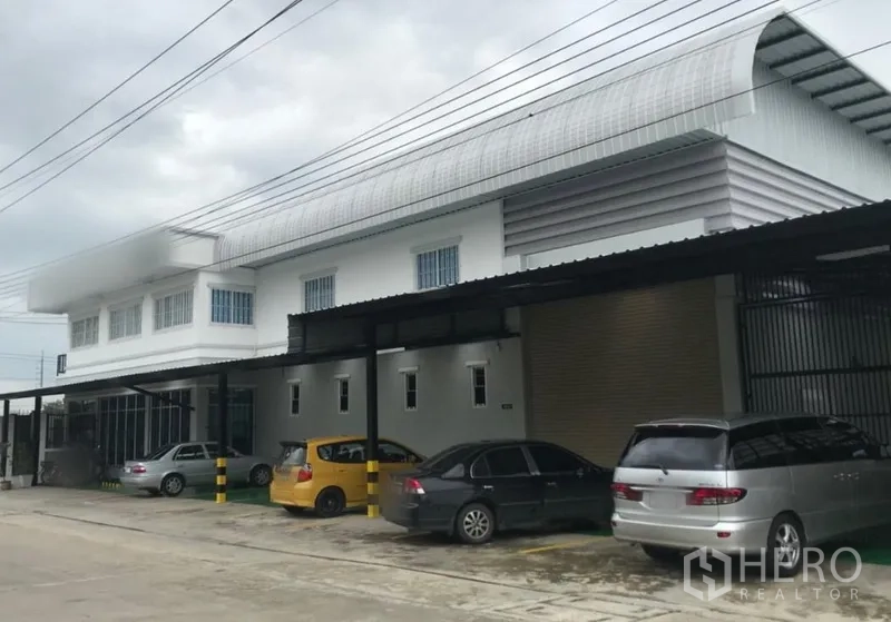 工厂 出租在Thanyaburi, Pathum Thani - 白色现代工厂，弧形屋顶，带顶装卸区与大型卷闸门，门前宽阔车道和停车位，位于Thanyaburi。