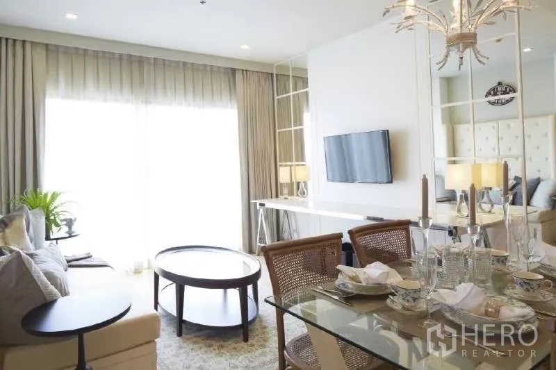 Condominium for rent in Bangkok - Dining area overlooking bright living room with TV, balcony glazing and sheer curtains.