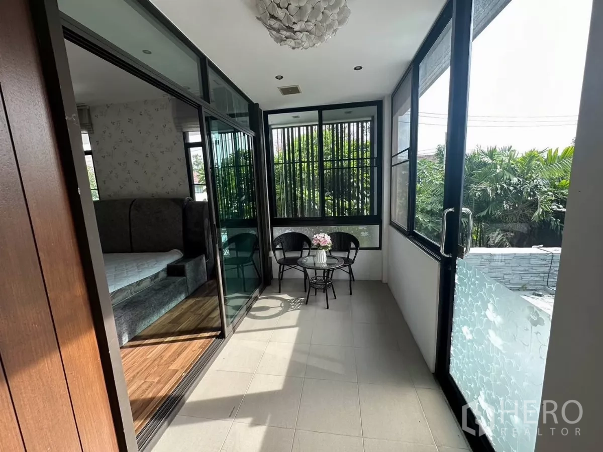 Detached House for rent or sale in Bang Kapi, Bangkok - Enclosed balcony sunroom with small table and chairs overlooking greenery.