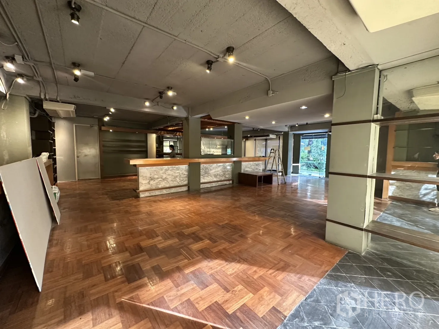 Retail Space for rent in Watthana, Bangkok - Large retail hall featuring a marble‑faced counter, wood floors, shelving, and garden views.