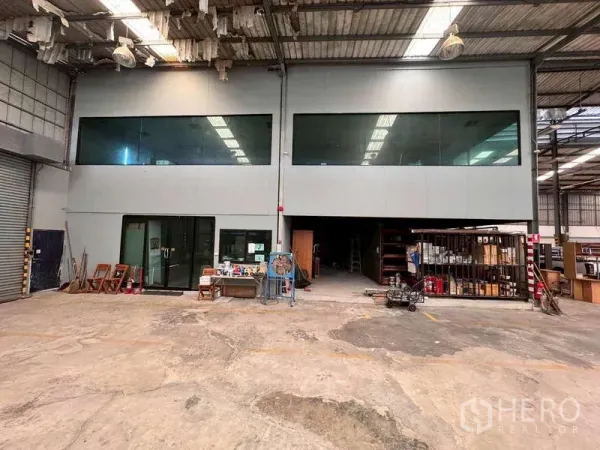 Warehouse for rent in Prawet, Bangkok - Spacious warehouse interior with mezzanine glass-walled office and concrete floor.