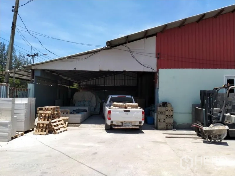 Warehouse for rent or sale in Lam Luk Ka, Pathum Thani - Covered loading bay beside the main warehouse with a pickup truck, pallets and storage materials.
