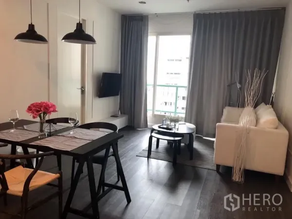 Condominium for rent in Pathum Wan, Bangkok - Open-plan living and dining area with dark wood floors, sofa, wall-mounted TV, and balcony doors.