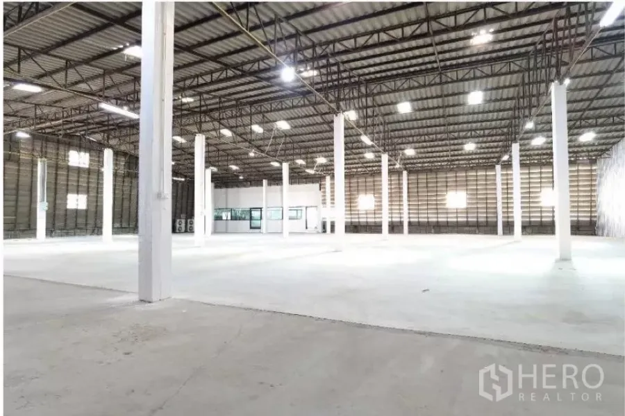 Warehouse for rent in Mueang Samut Prakan, Samut Prakan - Wide-span warehouse interior with high steel truss roof, bright lighting, white columns, and attached office.