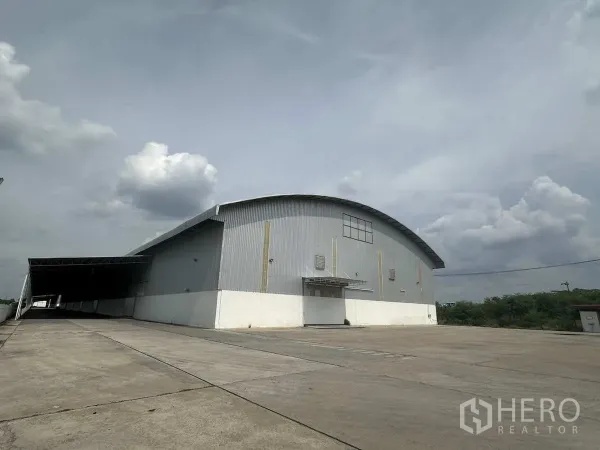 Warehouse for rent in Bang Pa-in, Phra Nakhon Si Ayutthaya - Large metal-clad warehouse with curved roof and expansive concrete yard under cloudy sky in Bang Pa-in, Ayutthaya.