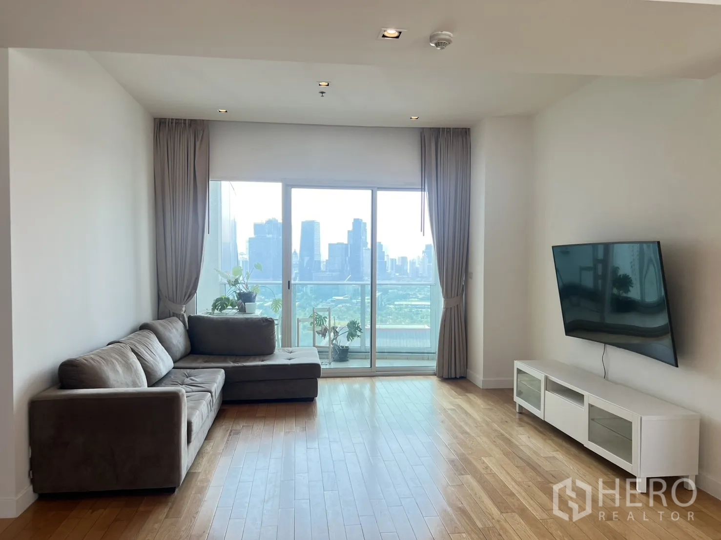 公寓 for sale in Khlong Toei, Bangkok - 客厅设L型沙发，阳台推拉门，远眺城市与公园景观