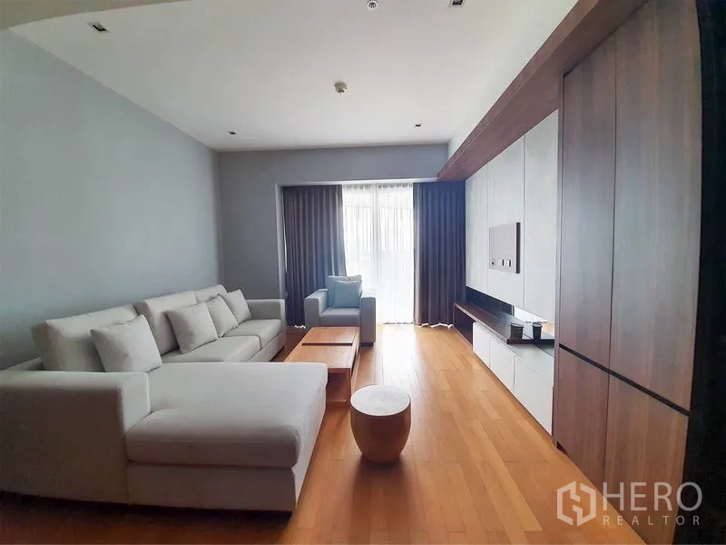 公寓 出租在Yan Nawa, Bangkok - 明亮客厅，L形沙发、木地板与电视墙，通向带窗帘的阳台。