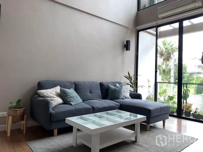 联排别墅 出租在Khlong Toei, Bangkok - 温馨客厅，转角沙发、玻璃茶几，推拉门通往阳台。